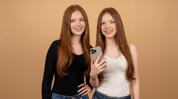 Letizia and Emilia Macula in smiling in front of a light-beige backgrounbd. EMilia holding an iPhone