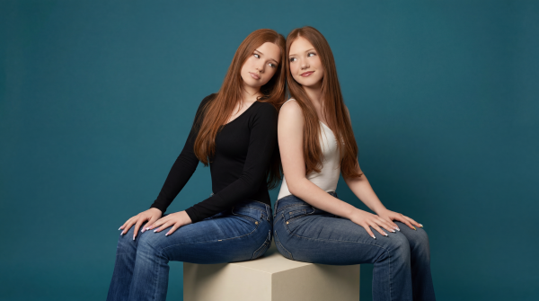 Letizia and Emilia Macula sitting on a light-gray cube in front of a blue background