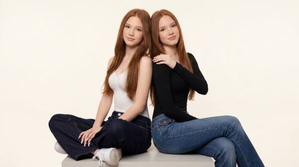 Emilia and Letizia sitting in front of a white background on a cube