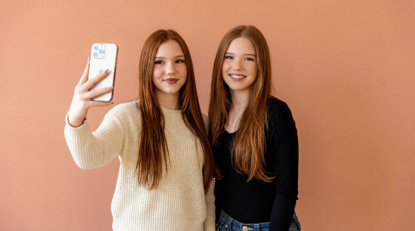 Emilia and Letizia Macula making a selfie and Photo with an iPhone in front of a red-orange background