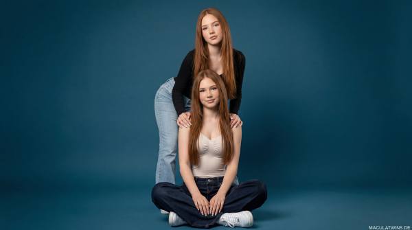 Emilia and Letizia Macula in front of a dark-blue background. Emilia sitting on the floor and Letizia standing behind her
