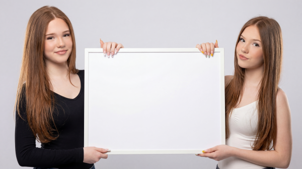 Emilia and Letizia in front of a light-gray background, holding a blank canvas