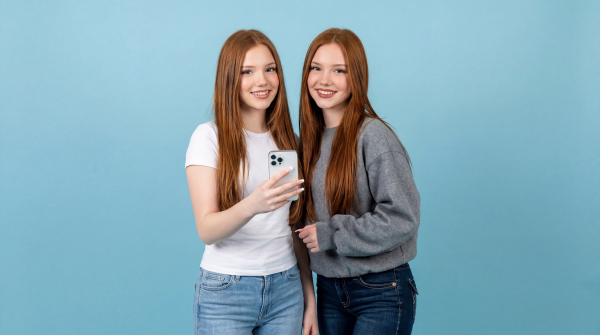 Emilia and Letizia holding a White iPhone. Standing in front of a light-blue background.